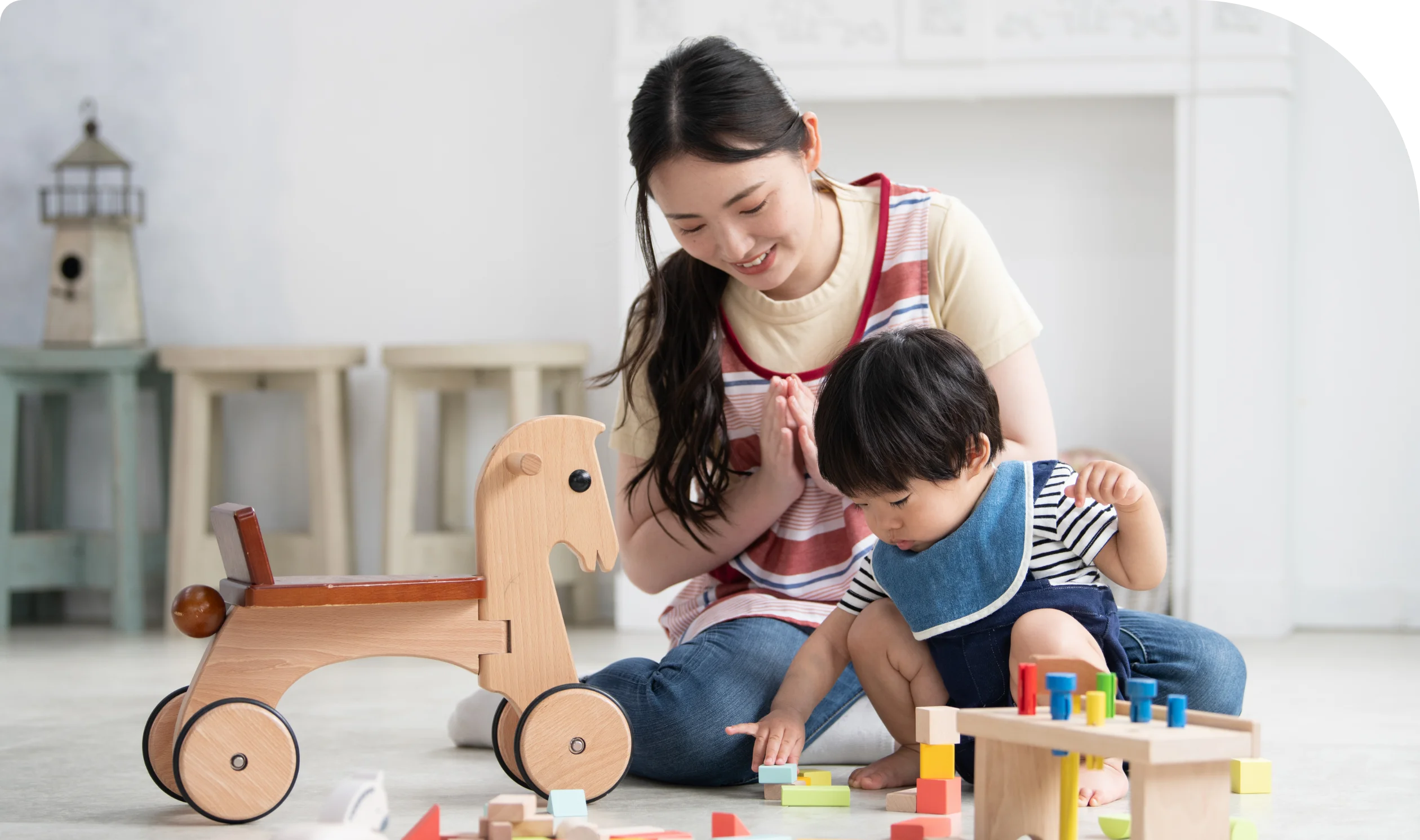 積み木などの木でできた知育おもちゃで遊んでいる幼児とそれを見守る保育士
