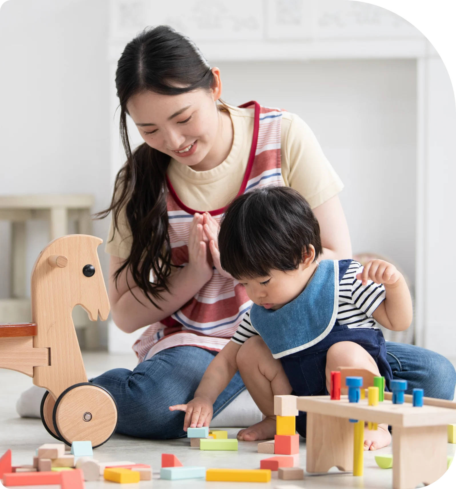 積み木などの木でできた知育おもちゃで遊んでいる幼児とそれを見守る保育士